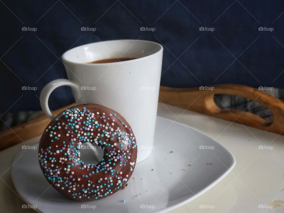 Enjoying a cup of coffee and a homemade chocolate donut with sprinkles.