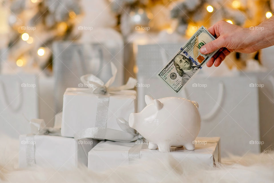 piggy bank with 100 dollars banknote in festive New Year atmosphere of scenery. Magical bokeh with Christmas tree and bright lights.