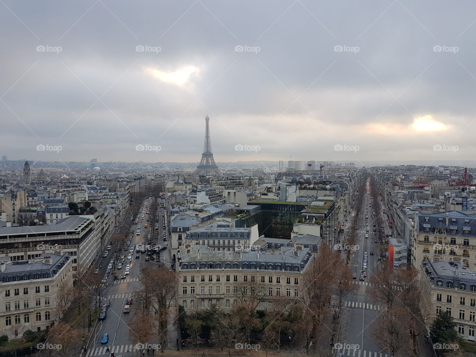 View from above the Arc de Triomphe, looking out to the city of Paris, France, Europe, with streets below and the Eiffel tower in the distance. Sun shines through clouds during the day in winter season, December.