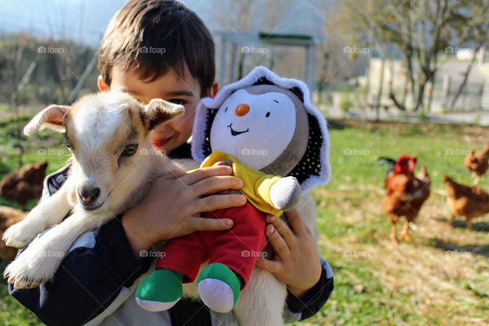 Little boy holding his toy and a small white lamb