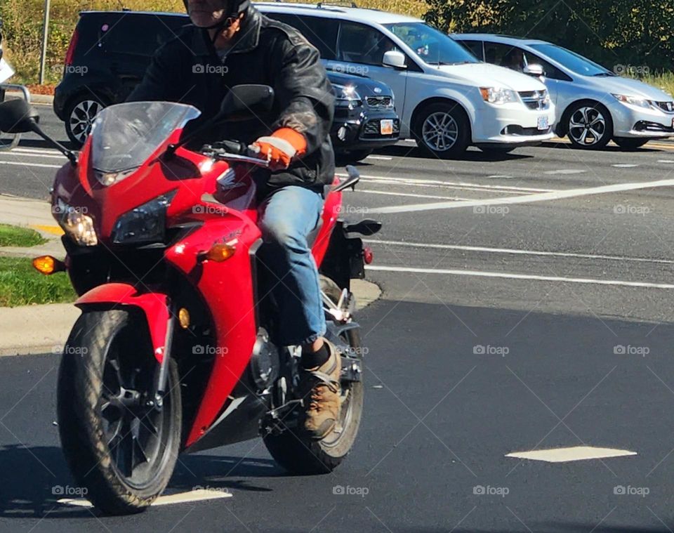 man riding a red motorcycle toward the camera in commuter traffic on a sunny afternoon in Oregon