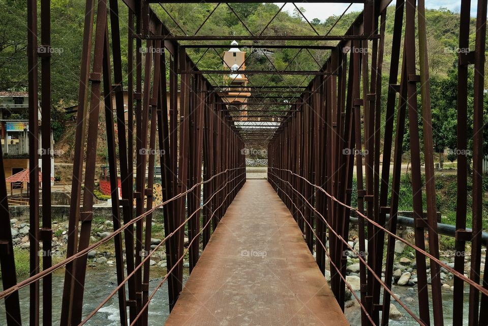 Red steel bridge with church in the background over rushing river