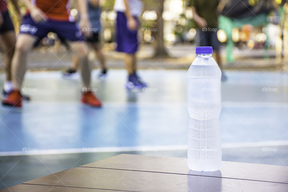 Bottle of drinking water on the wooden chair Background Blurry image of people playing basketball on a court.