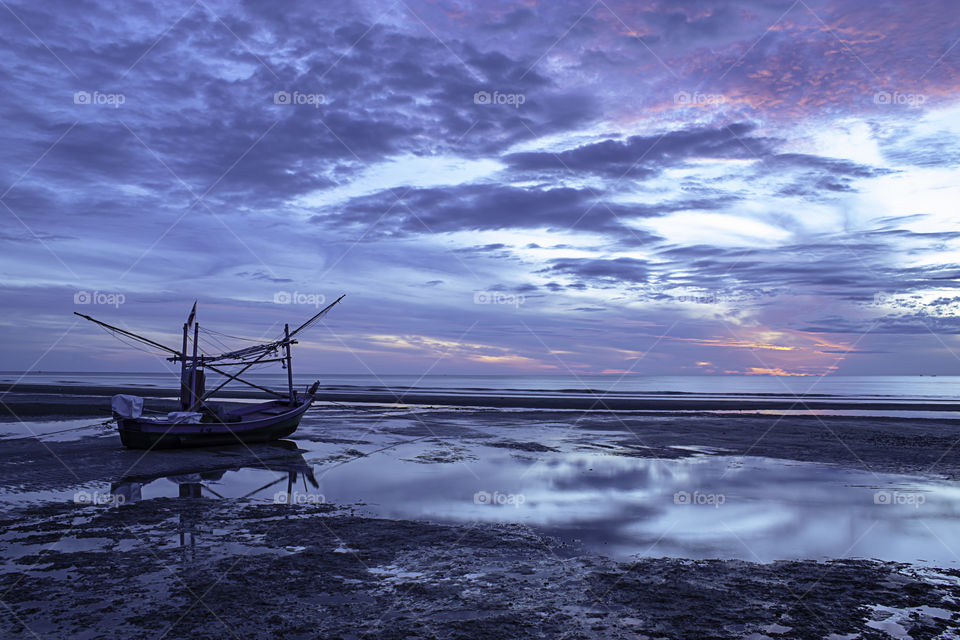 The morning sun light in the sea and the boat on the beach.