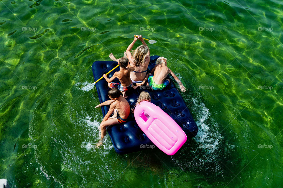 Happy family with children is swimming and having fun in the sea on a inflatable matress. Aerial view.