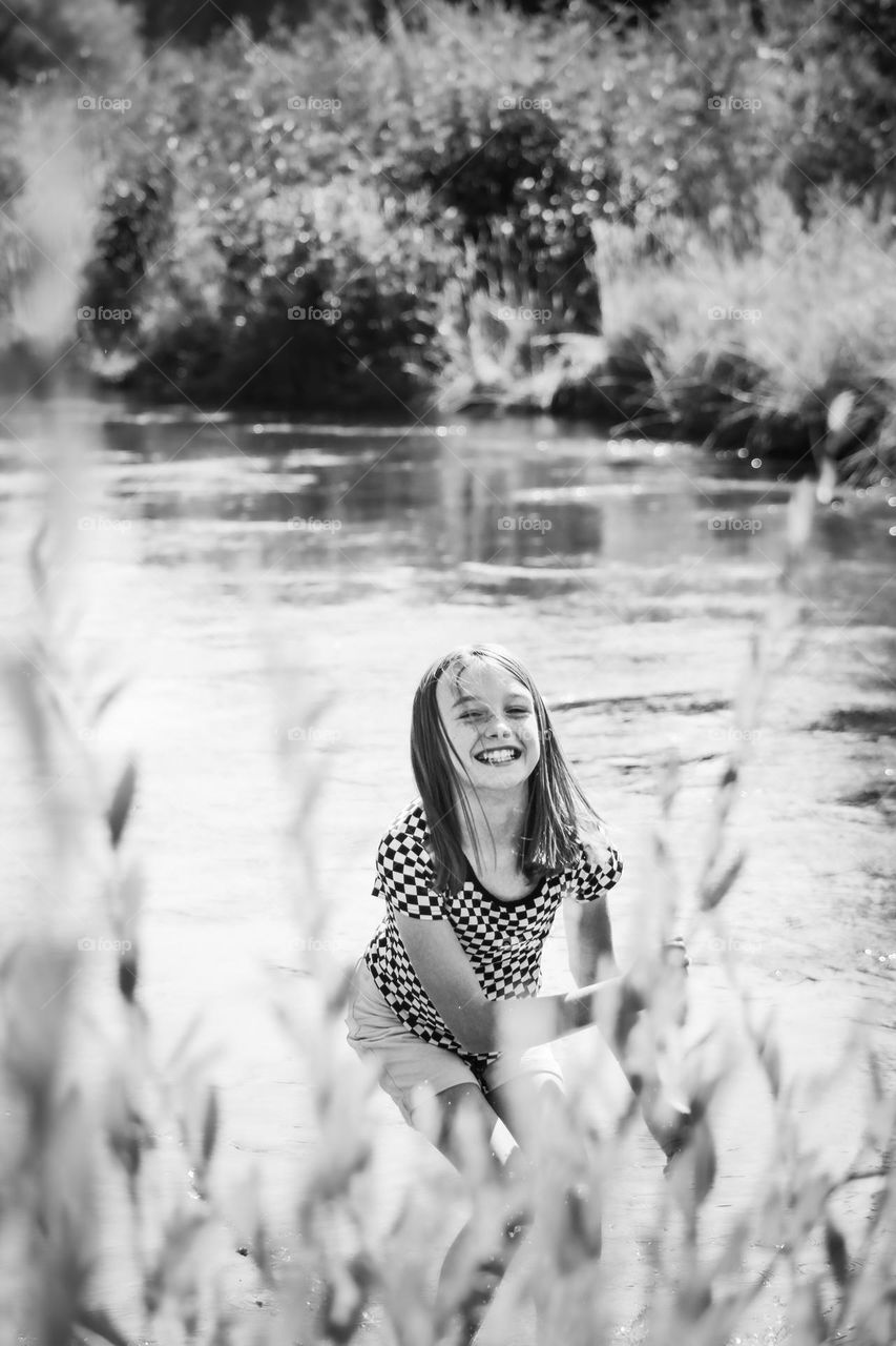 Black and white photo of a smiling young girl in front of a river on a nice hot summer day 