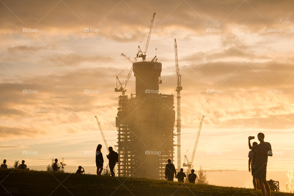 silhouette under construction high-rise building with cranes and silhouettes of people walking near