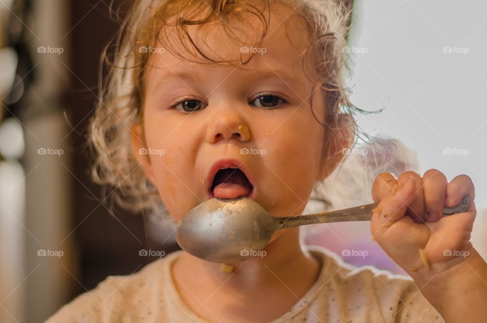 Child girl holding spoon near her messy face