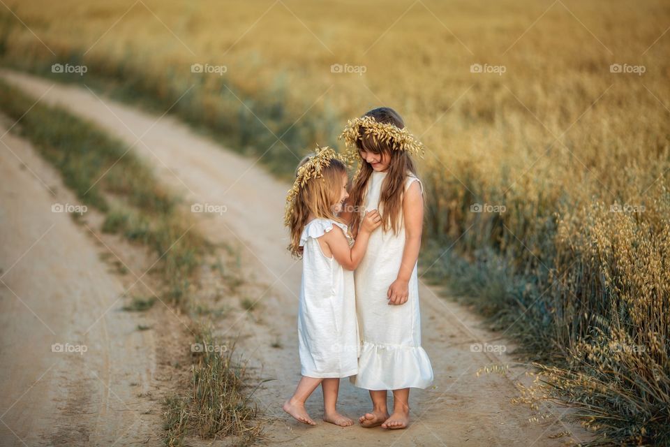 Little sisters in rye field at summer evening 