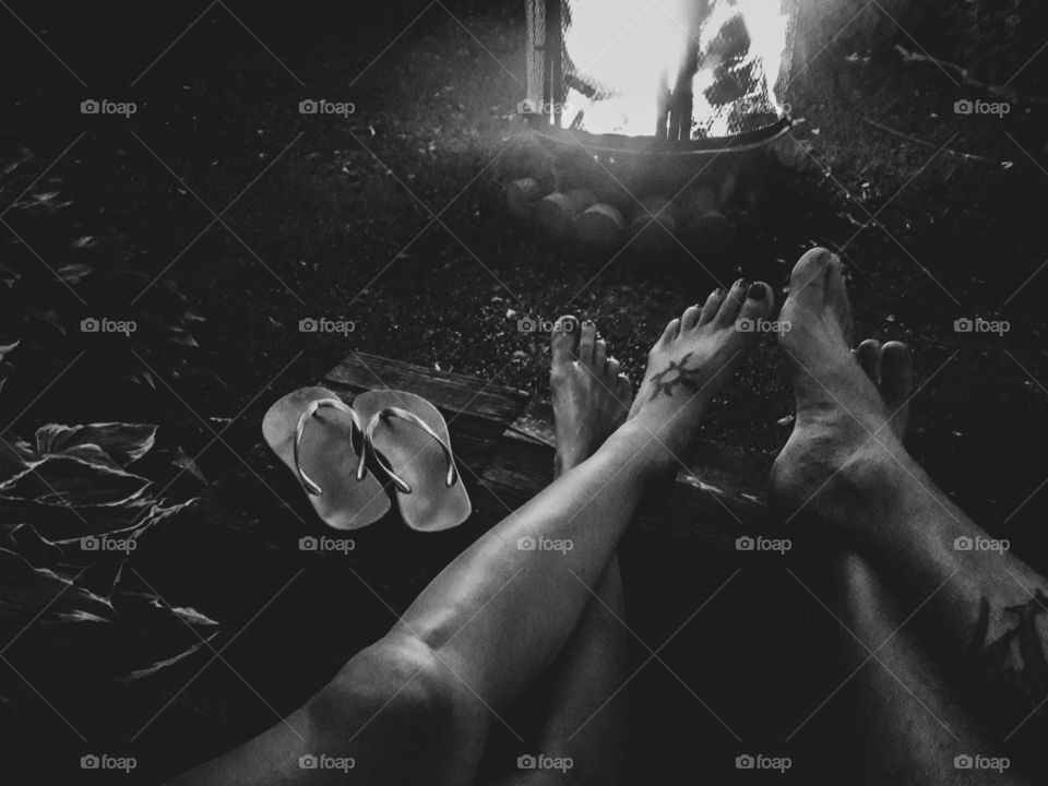 Black and white photograph of two people with their feet up. Relaxing by a bonfire on a summer night.