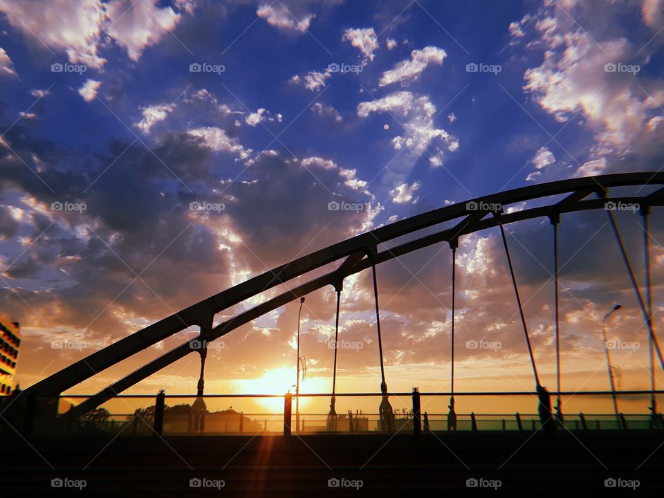 Just beautiful sunset and huge bridge. Amazing soft clouds and perfect blue sky. Evening summer city in sun lights