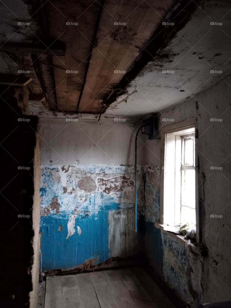 An old destroyed emergency room with a blue peeled-off wall with a window on the right with a wooden floor