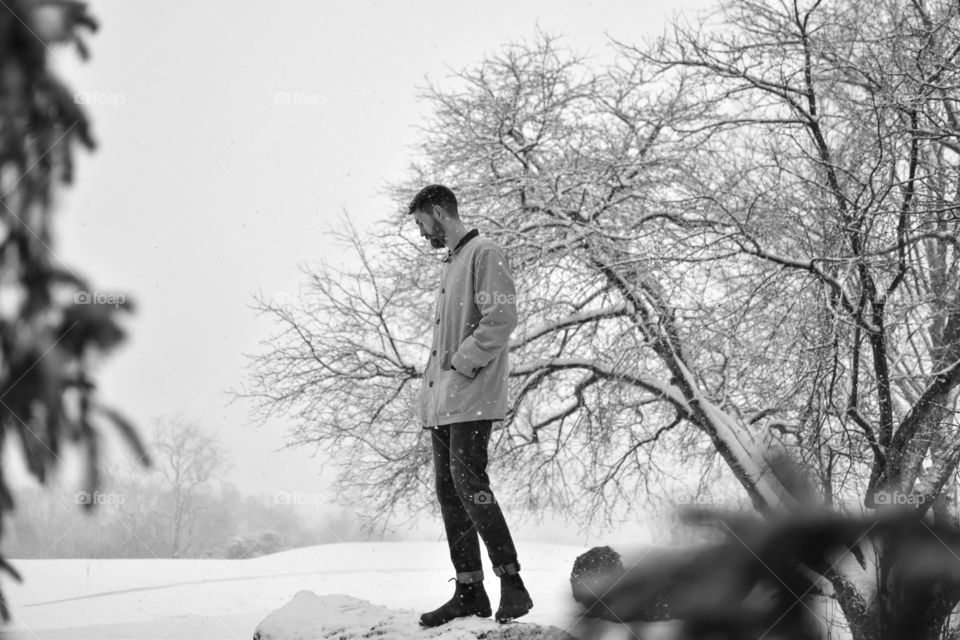Black and white image of model standing on a felled tree in the snow. 