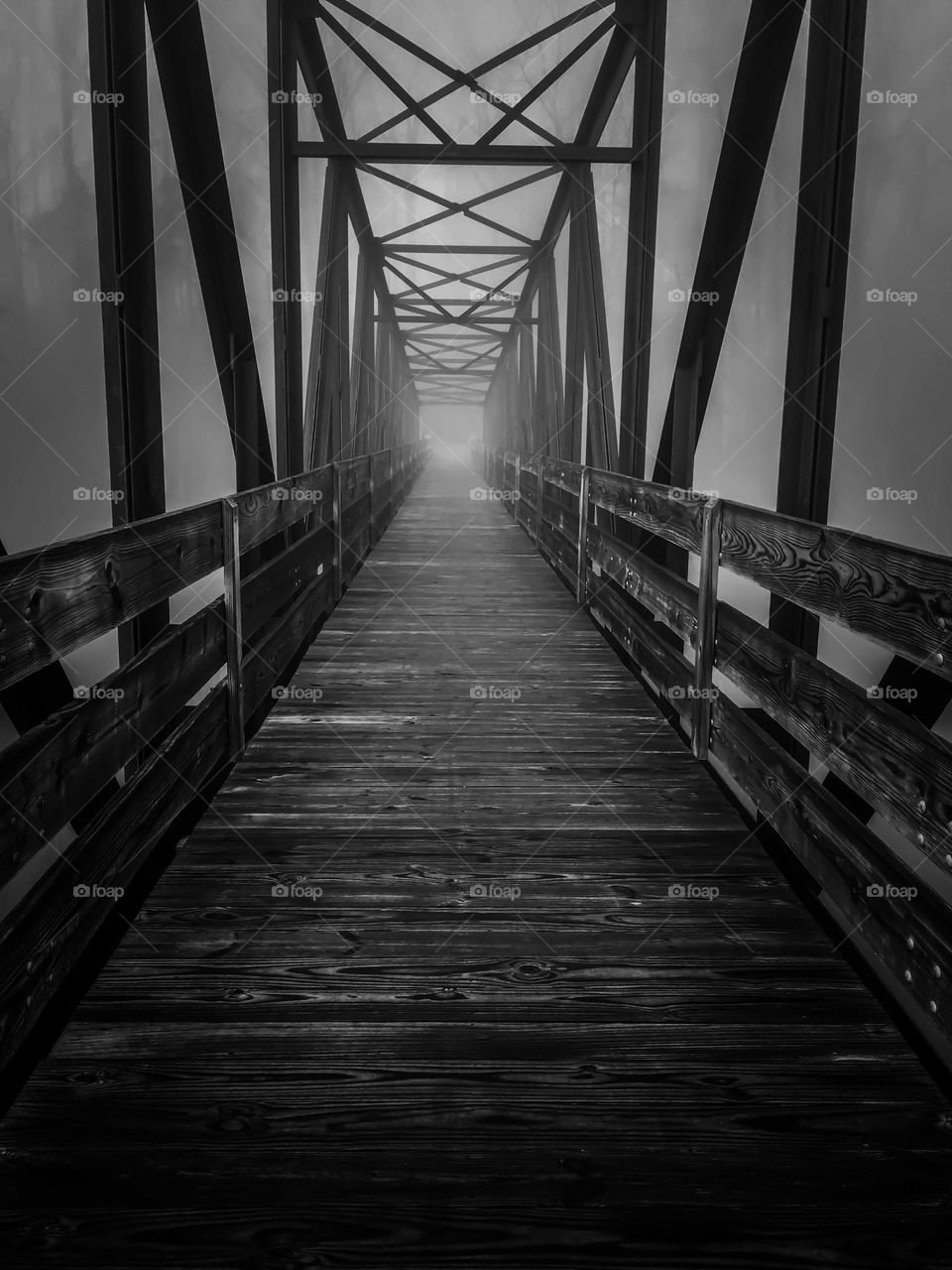 An eerie truss bridge leading into a mysterious fog. 