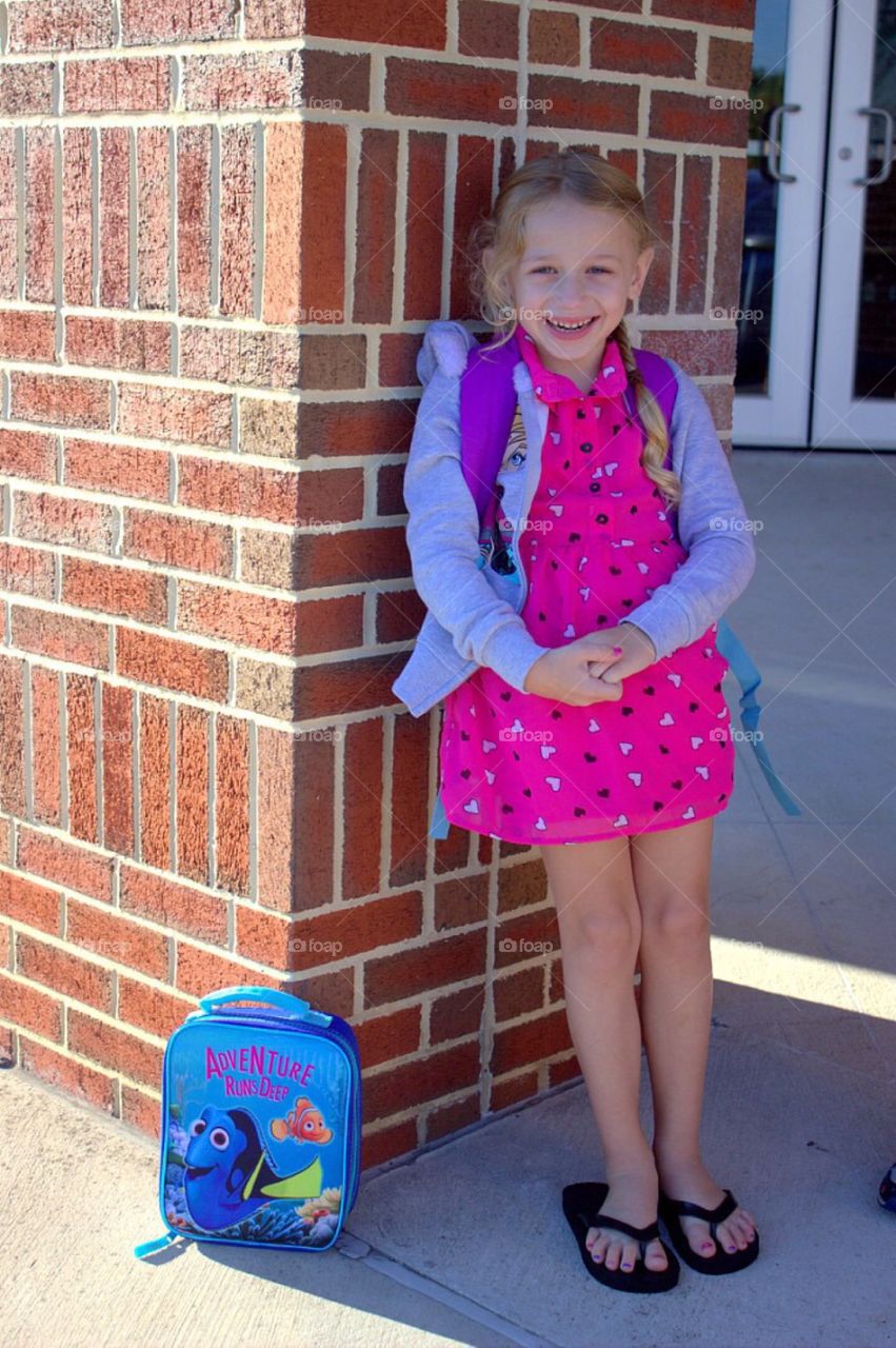 Smiling girl leaning on brick wall of school building