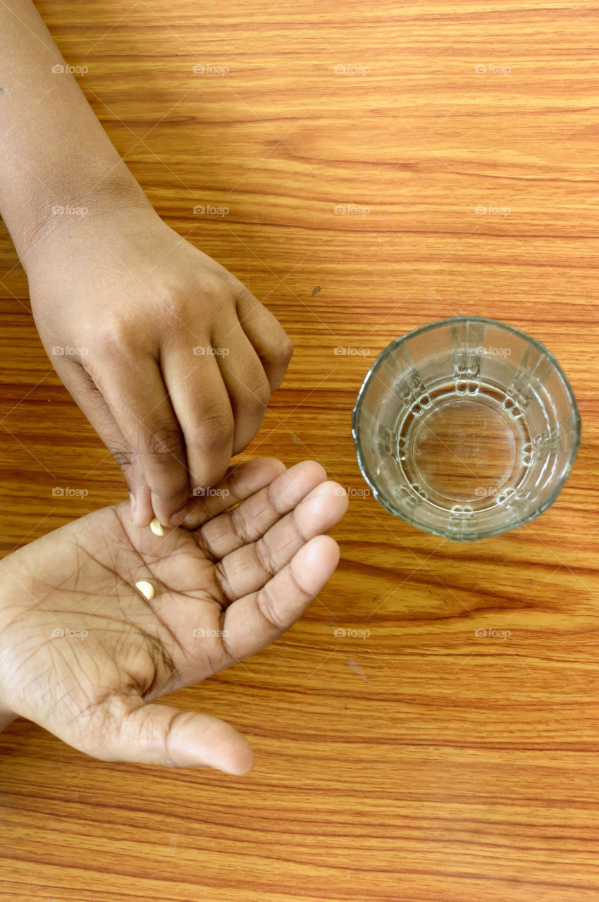 Self-treatment at home as per prescribed by doctor. A teenager boy pouring medicine into her hand. Medical, health care or people concept. High Angel view. Close up with copy space room for text.