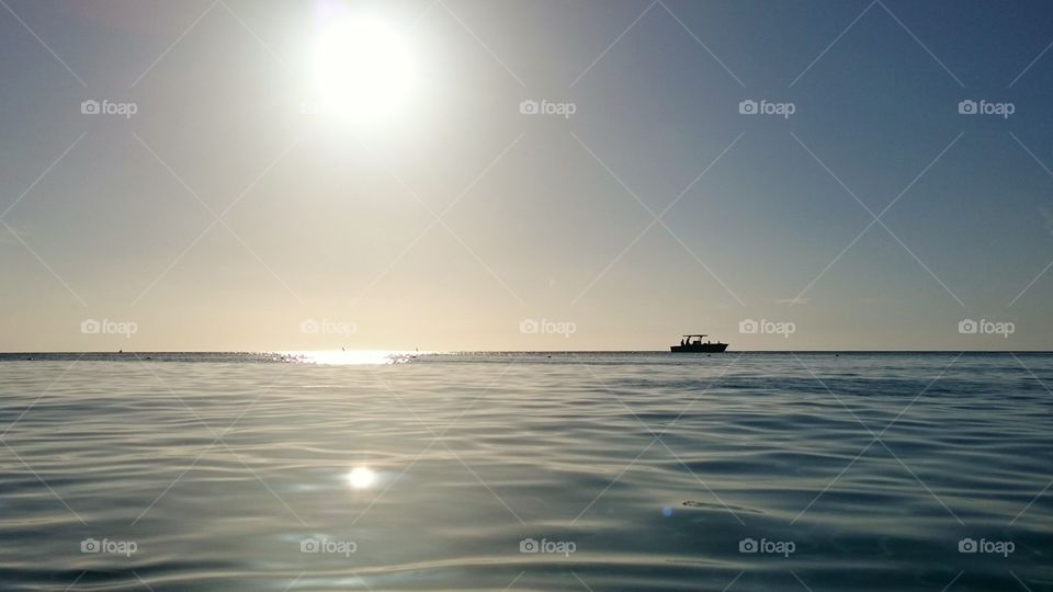 The horizon in the Distance. A small boat next to the sun reflected on water. A nice sunny day on summer.