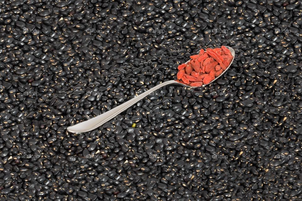 Dried fruits on spoon . Red Chinese wolf berries on spoon. Spoon surrounded by black beans. Frame filled with black beans. Dried berries