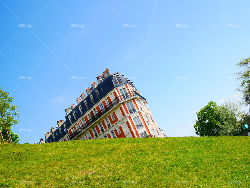 Tilted building on grass against sky