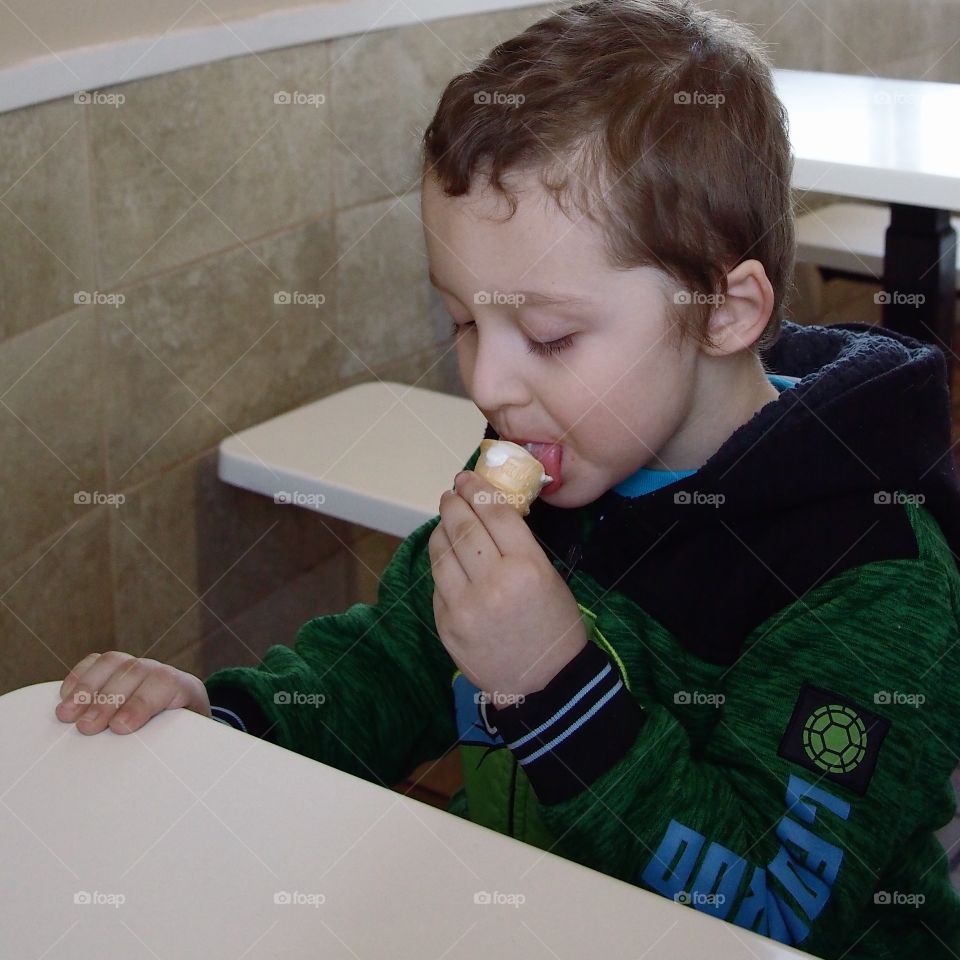 A little boy taking a bite of his vanilla ice cream cone. 
