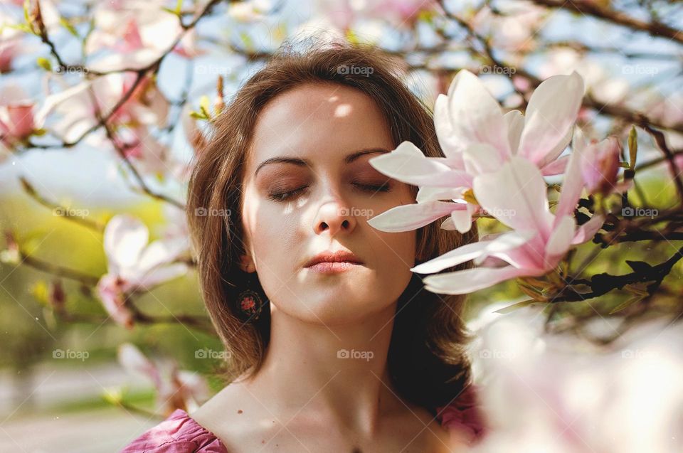 Portrait of beautiful young woman in garden with blooming magnolias close up. Spring time.