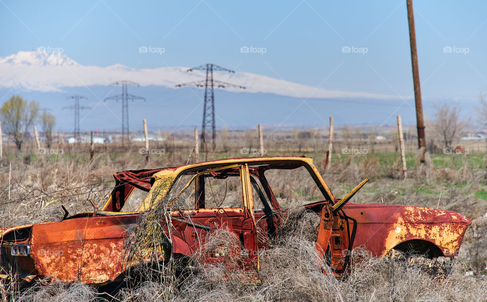 Abandoned and rusty wreckage of an yellow vintage Soviet Russian car in the middle of dry hay with scenic ice top mountains and clear blue sky on the background in rural Southern Armenia in Ararat province on 4 April 2017.