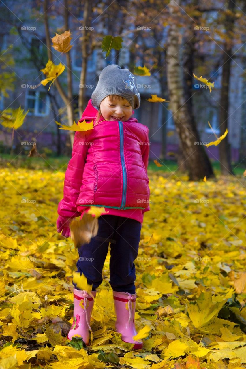 A child is playing witch the fallen leaves