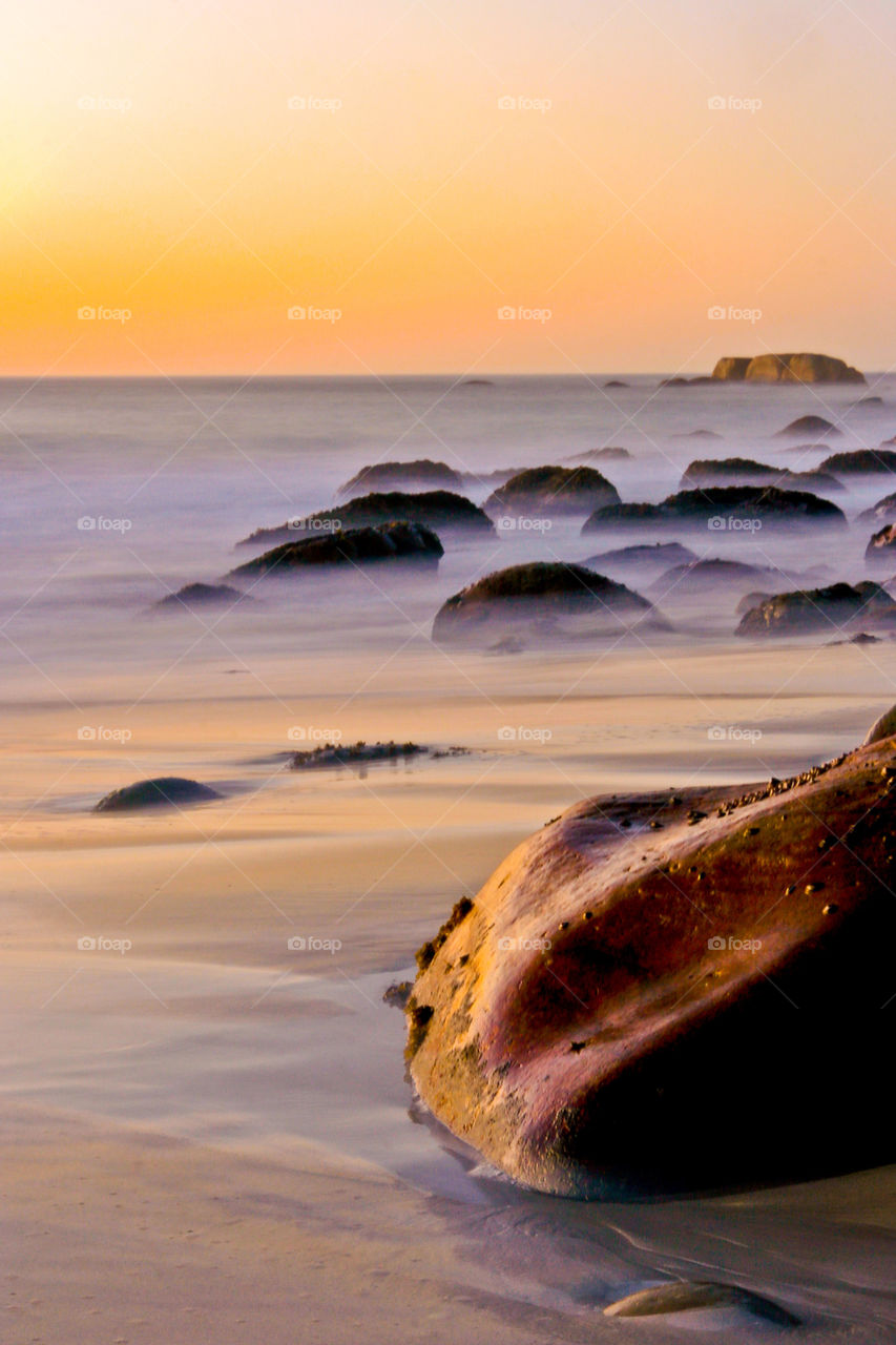 Love this dreamy seascape! Long exposure image with large rocks at sunset with waves between boulders.