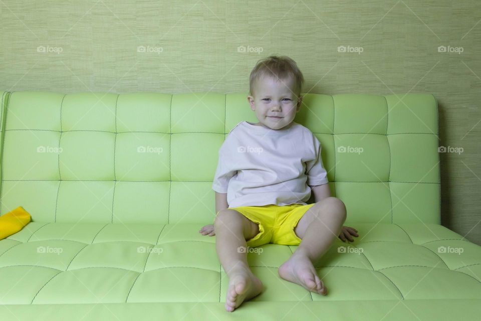 A portrait of a child sitting at home on a green sofa depicts different emotions in yellow shorts.