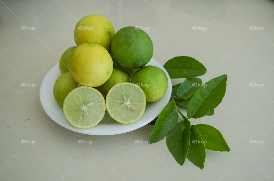 Plate on leaves is filled with yellow ripe, and green unripe limes, one of which is cut in halves