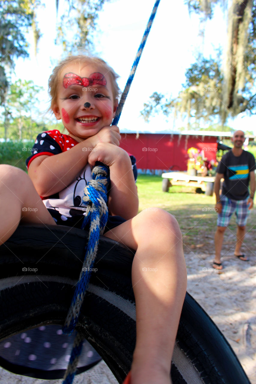 Happy girl with face paint enjoying swing in park