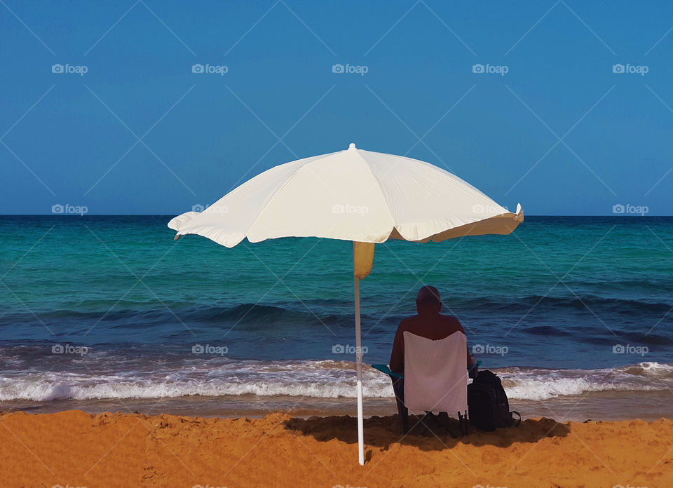 man on beach with turquoise sea and white umbrella