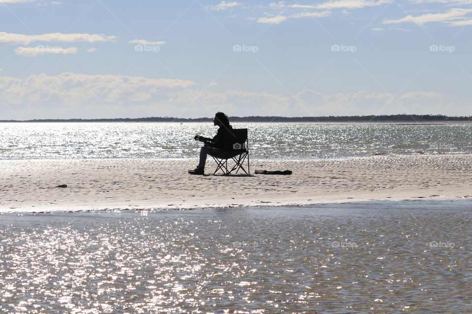A lone guitarist singer sitting in chair playing guitar at beach silhouette 