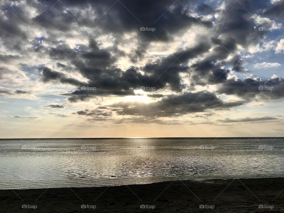 Dramatic cloudy sunset over the sea in Mauritius. Blue sky peeking through with golden sun rays over a calm sea 