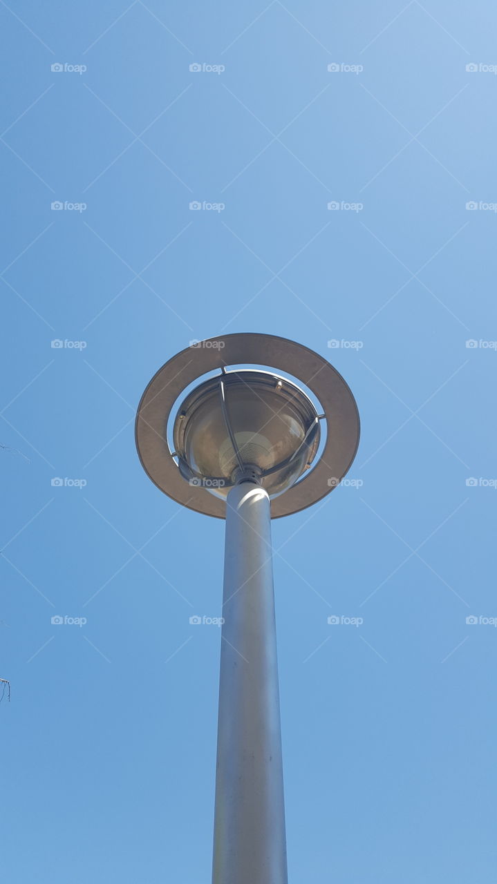 While in a parking lot, I  looked up and noticed the night street lamps they have closer to the shops. shiney metal against a nice blue sky.