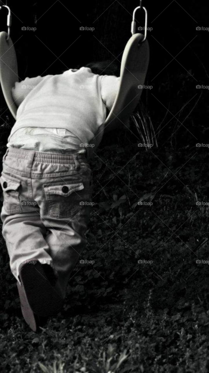 Toddler in saggy pants sulking on swing. black and white.