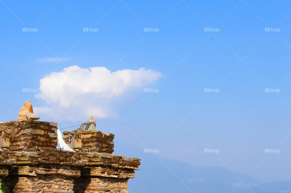 Old ruined Grit stone stone wall background against blue sky with cotton wool clouds and Kanchenjunga mountain range. Rabdentse Ruins, West Sikkim, India. Copy Space.
