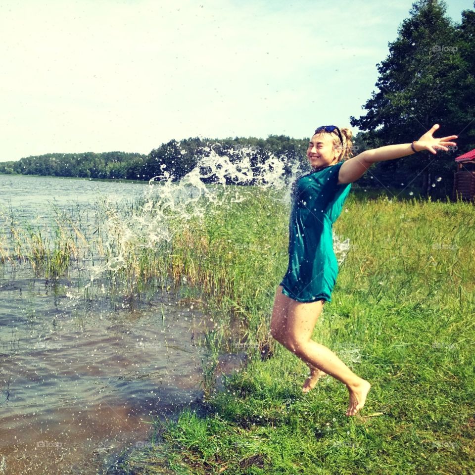 Девушка возле озера с летящей водой в нее , радость игры
