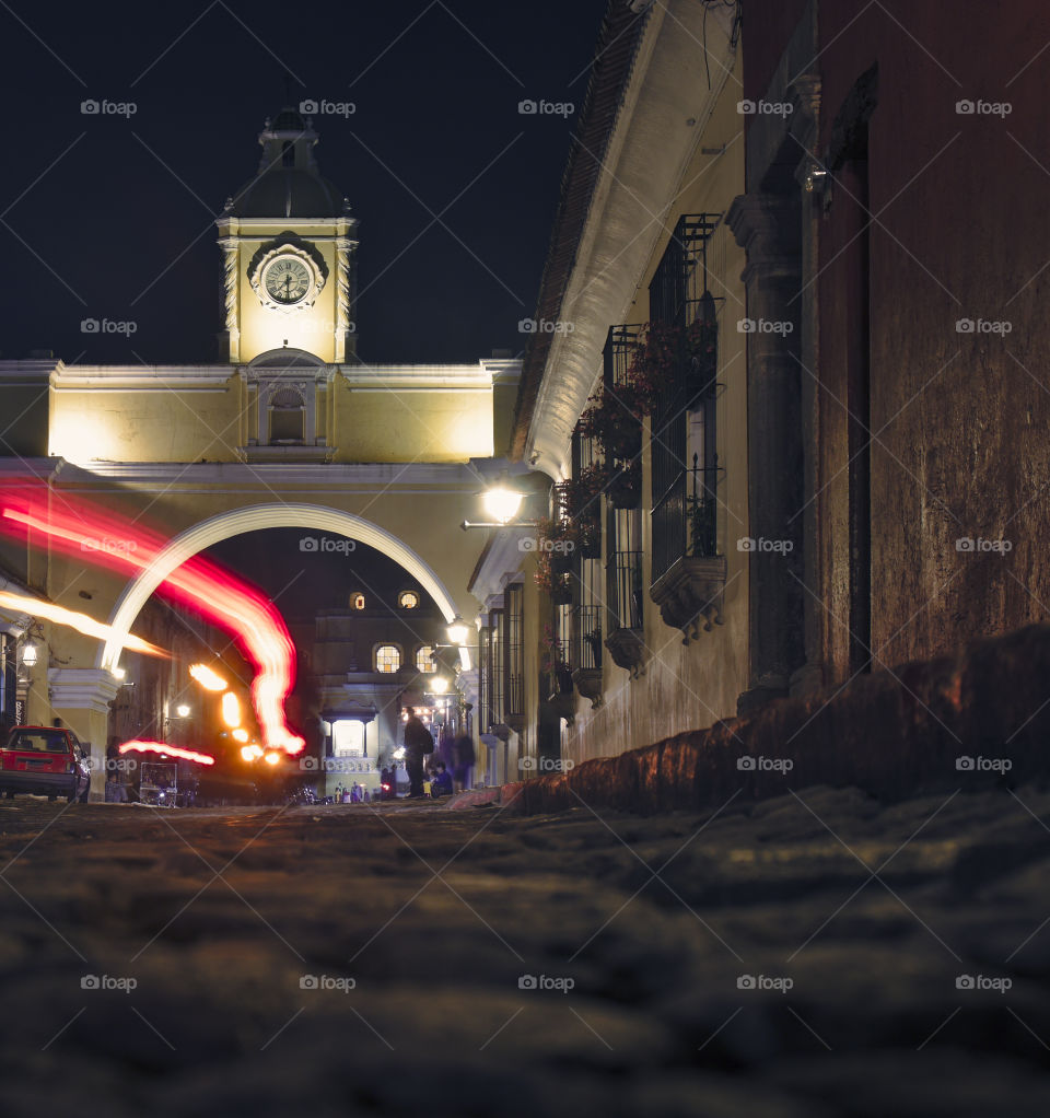 El arco in guatemala city (antigua) at night with light trail of motorcycle passing through arc.