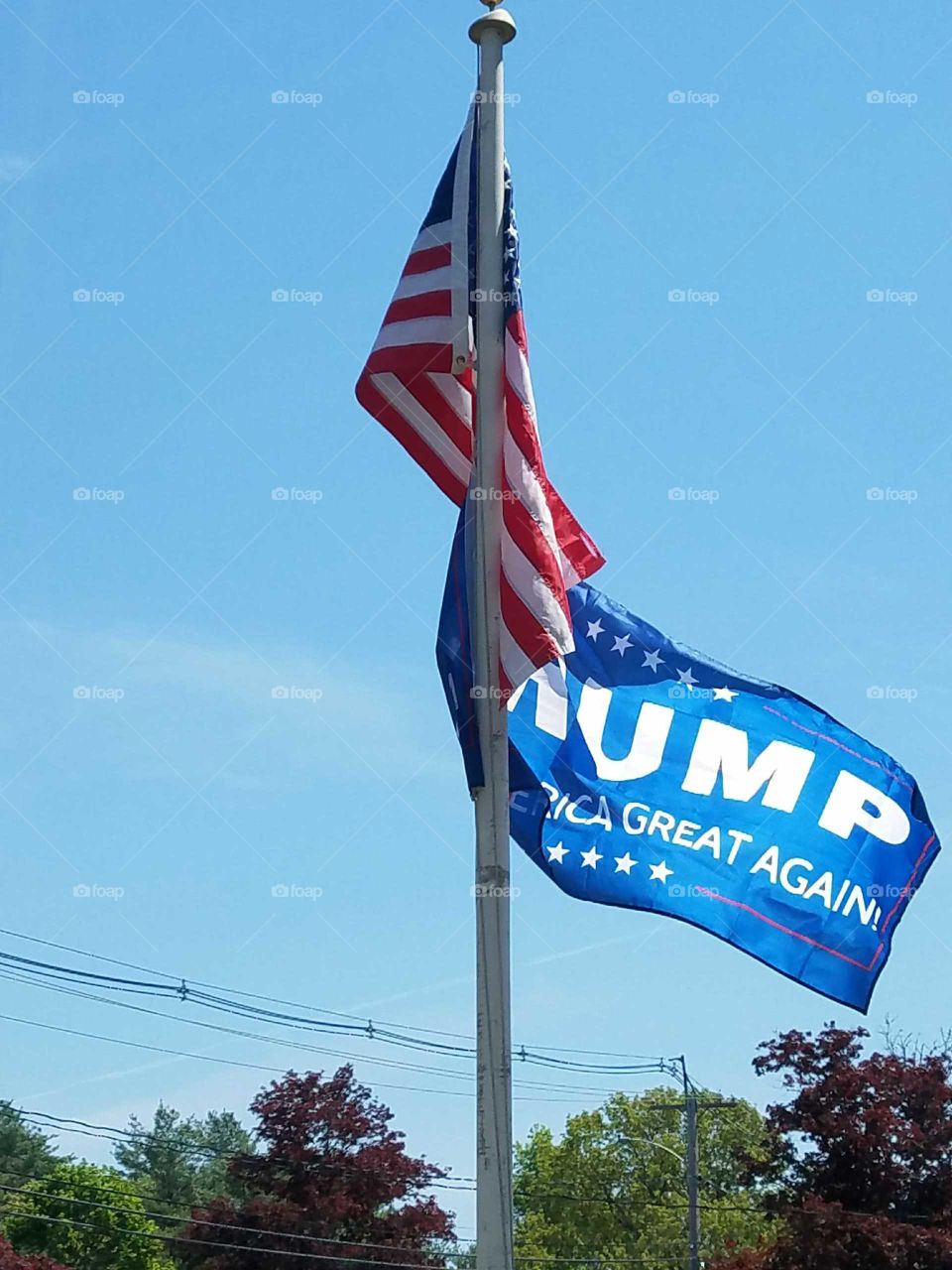 Trump flag & USA🇺🇸 flags on flagpole together, blue sky.