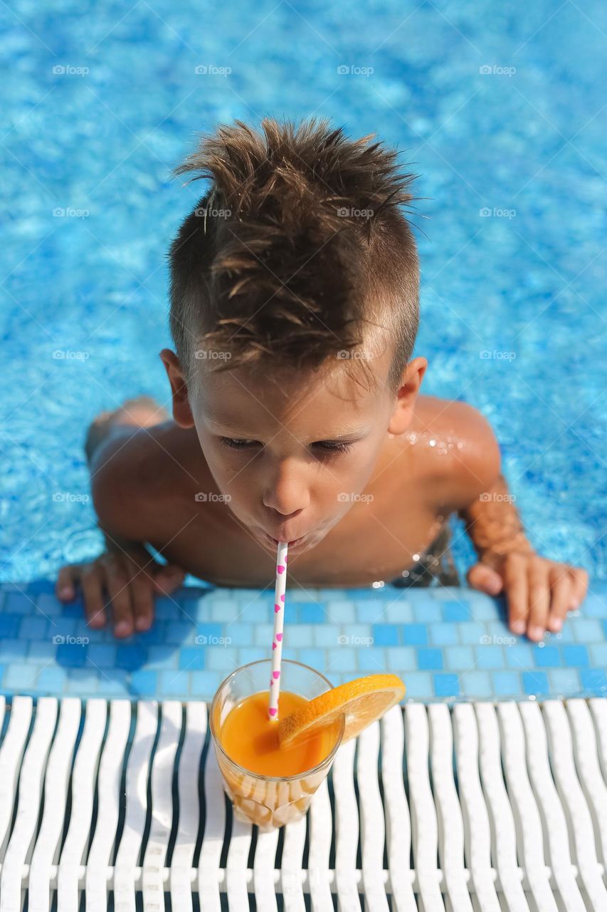 Little boy drink juice near the water-pool 