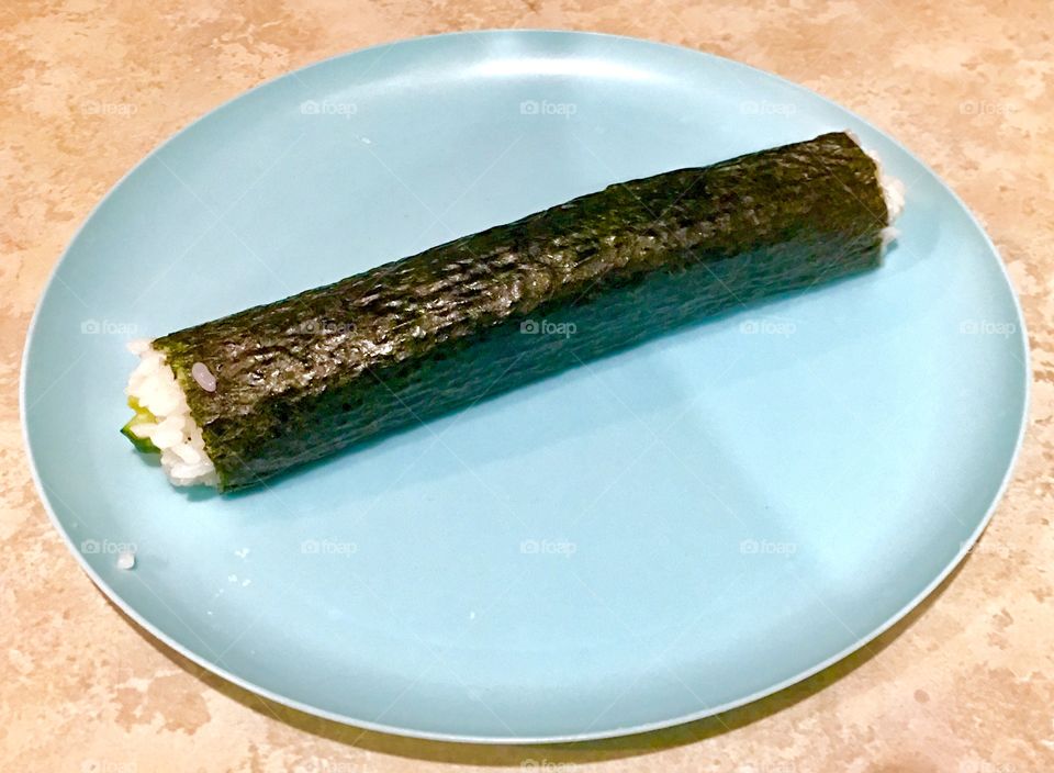 A Roll of sushi on a blue plate with rice spilling out of the ends