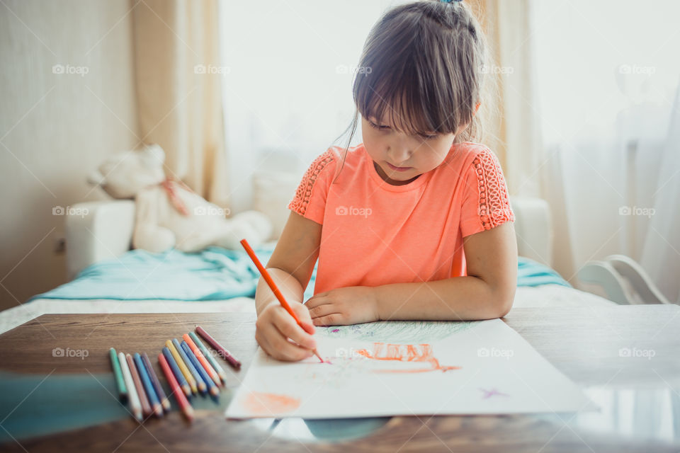 Little girl drawing with colorful pencils at wooden desk indoor