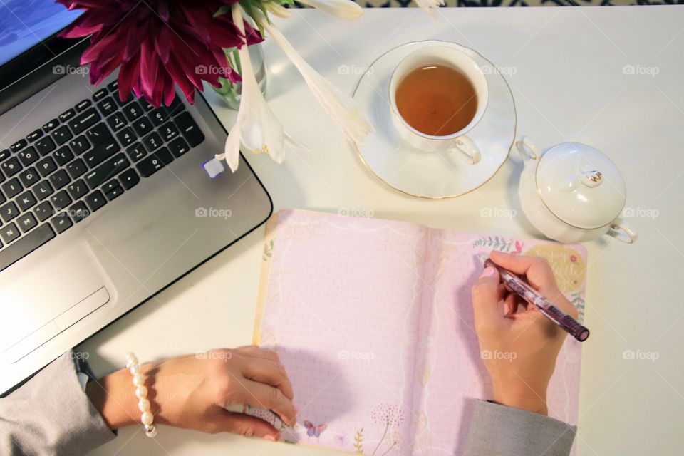 Female writing at desk with tea and laptop