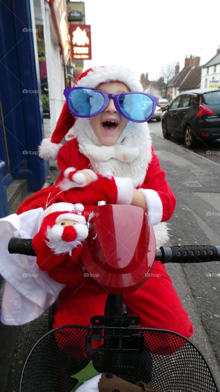 obscure sight of a girl dressed as father Christmas with jumbo sunglasses on a mobility scooter.