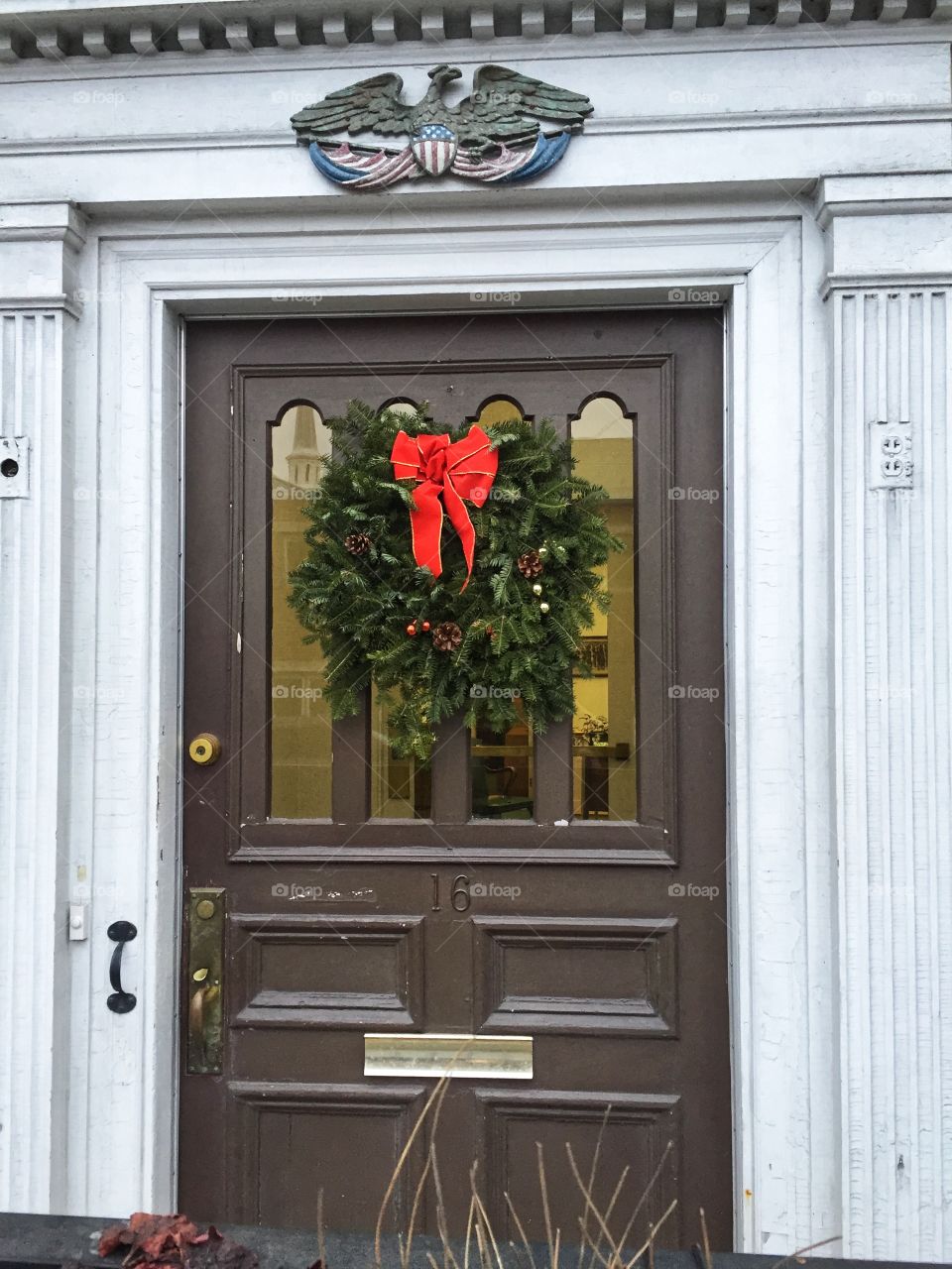This is a festive door decorated with a Christmas wreath. The door is brown and the wreath is green with red accents.