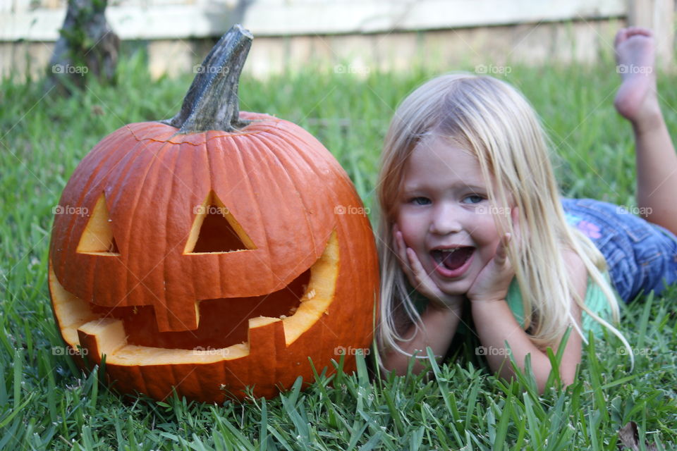 Little girl lying on a grass with halloween pumpkin