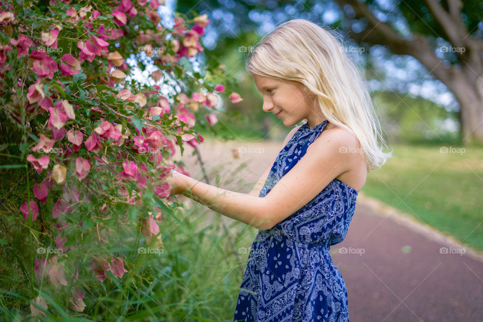 Beautiful blonde little girl admiring the flowers along a rural country trail set in Honolulu 