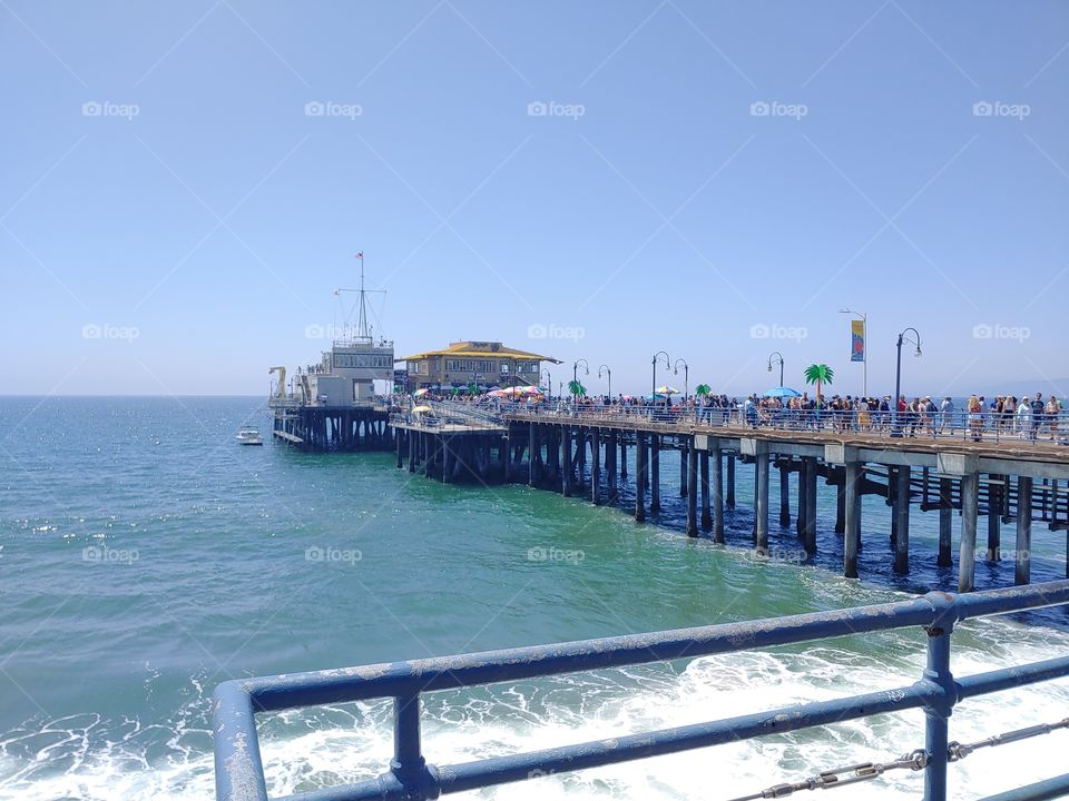 Photo shows clear blue skies and the boardwalk at Santa Monica Beach Pier