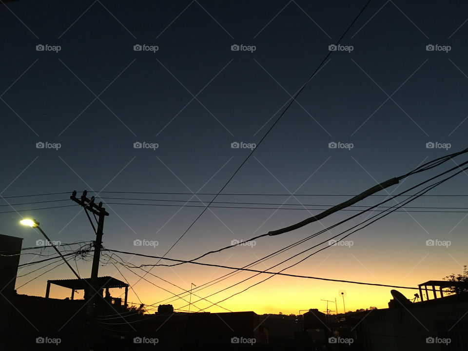 Sunset in a remote neighborhood of São Paulo, Brazil, america do sil, with electricity wires, water tank and roofs appearing in the golden backlight
